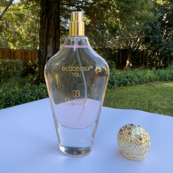 Open DELICIOUSLY YOU perfume bottle with cap placed beside on white surface.