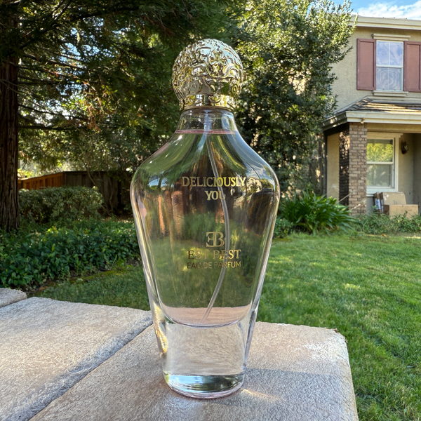 DELICIOUSLY YOU perfume bottle standing on stone surface in a garden setting.